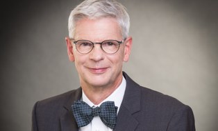 Portrait of a man with grey hair, glasses, suit and bow tie