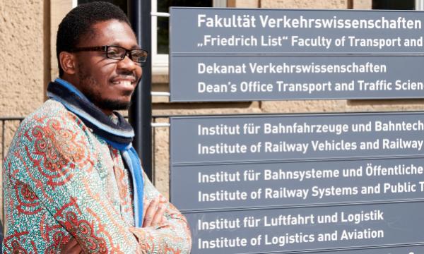 A man stands next to a TU Dresden sign