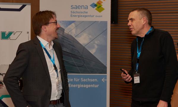 Two men are talking animatedly in front of posters.