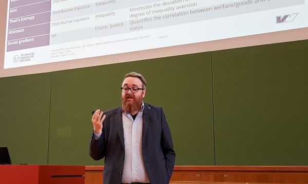 A man gives a lecture in a lecture hall in front of a blackboard