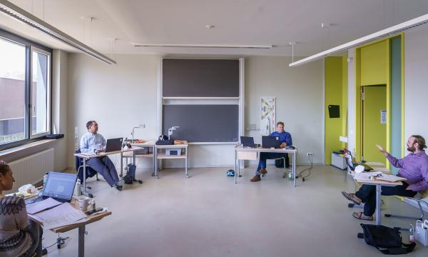 Three men and one woman in a classroom diskussing with eachother.