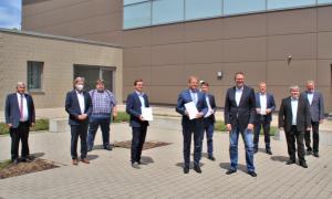 Line-up for the media representatives: Handover of the expert report by Prof. Arnd Stephan (5th from left) and two of his research assistants, Johannes Strohhäcker (l.) and Jan Pape (r.). 10 men in suits stand in front of a building. Two are holding a document in their hands.