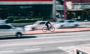 Ein Mann fährt schnell Rad in Großstadt. Um ihn herum sind Autos.