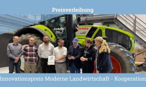 5 men and 2 women stand in front of a tractor. One man is holding a prize, another a certificate.