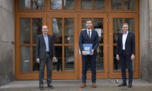 Drei Männer stehen vor der großen Holzeingangstür der Fakultät Verkehrswissenschaften.