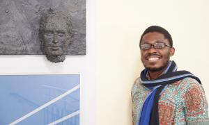 Humboldt Stipendiat Jack Asare Awuku aus Ghana im Potthoff-Bau der TU Dresden neben einem Wandrelief von Friedrich List, den Namensgeber der Fakultät Verkehrswissenschaften. Ein Mann steht neben einem Wandrelief von Friedrich List