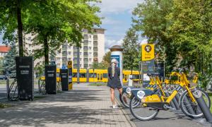 Im Hintergrund eine Tram, rechts parken E-Bikes, links sind Stromtankstellen, mittig eine Frau