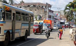 Eine volle Straße in Srki lanka mit einem Bus, Autos, ein Motorrad, eine Frau und Kuh am Straßenrand