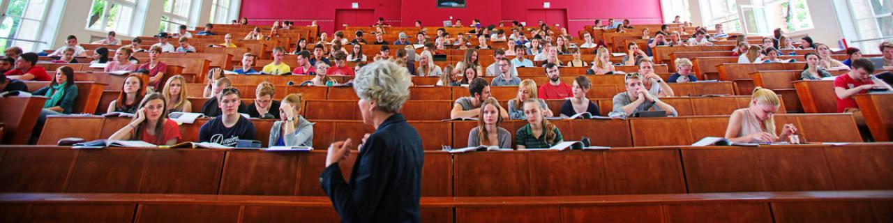 Das Foto zeigt einen Hörsaal voller Studierender. Im Vordergrund erkennt man die Dozentin.