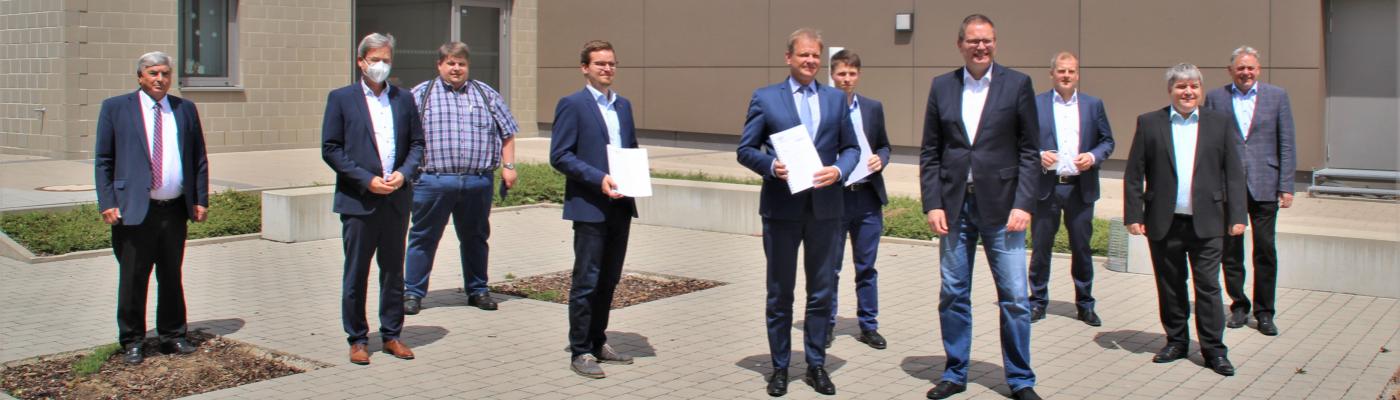 Aufstellung für die Medienvertreter: Übergabe des Gutachtens durch Prof. Arnd Stephan (5.v.l.) und zwei seiner wissenschaftlichen Mitarbeiter, Johannes Strohhäcker (l.) und Jan Pape (r.) 10 Männer in Anzügen stehen vor einem Gebäude. Zwei halten ein Dokument in Händen.