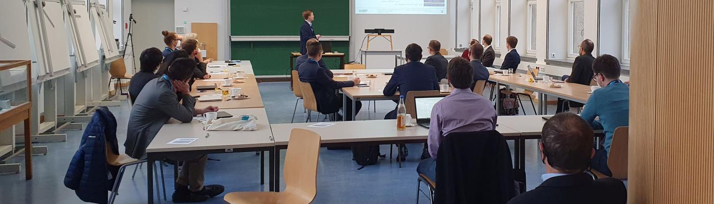 A seminar room with people. One of them is giving a lecture at the front.