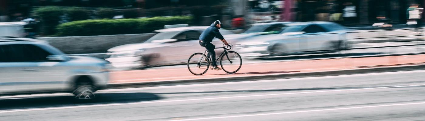 A man is cycling fast in a big city. Around him are cars.