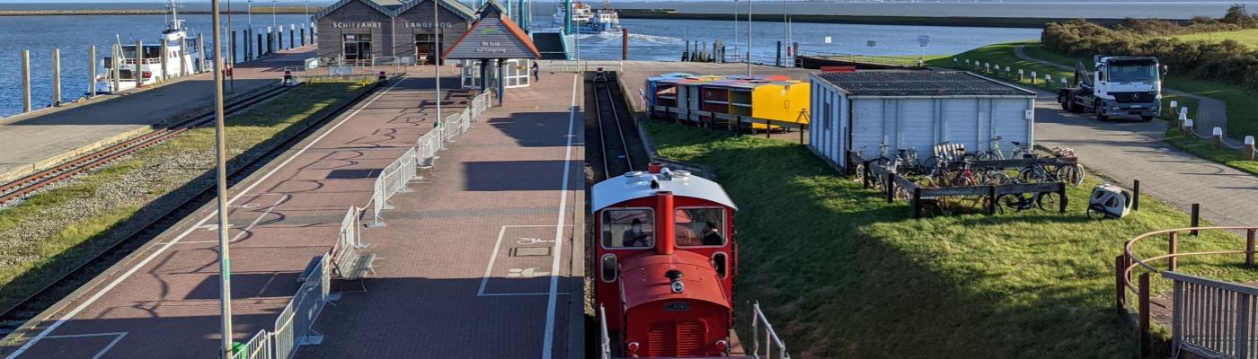 In the foreground is a railway, in the back a station and the North Sea