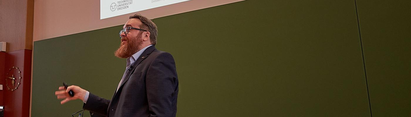 A man gives a lecture in a lecture hall in front of a blackboard