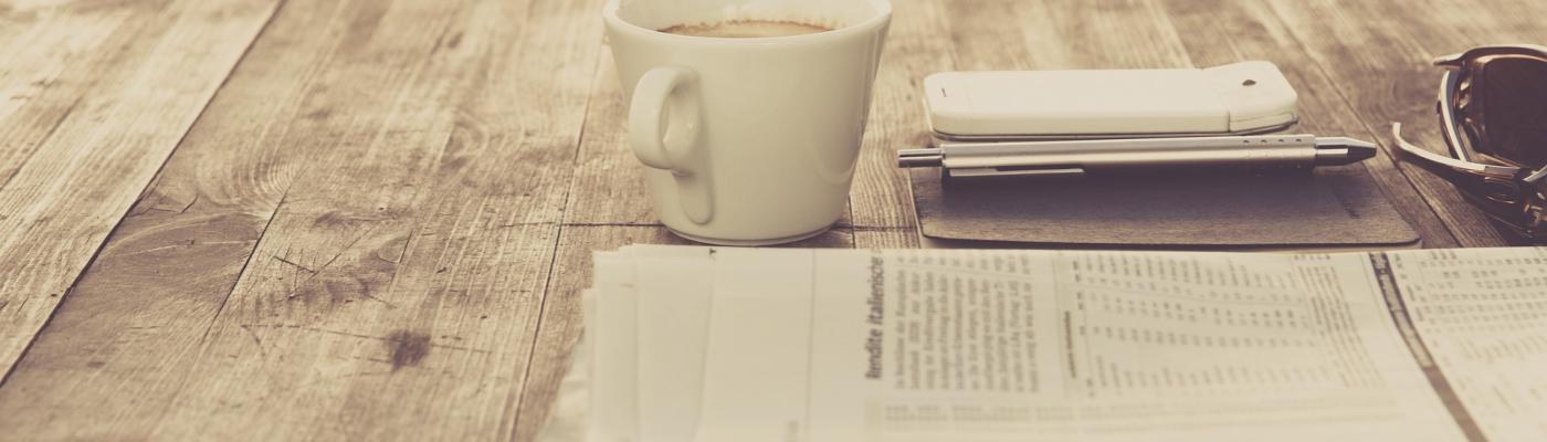 a newspaper lies on the table, next to it a cup of coffee.