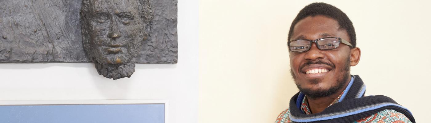 Humboldt Fellow Jack Asare Awuku from Ghana in the Potthoff Building of TU Dresden next to a wall relief of Friedrich List, who gave his name to the Faculty of Transport Sciences. A man stands next to a wall relief by Friedrich List