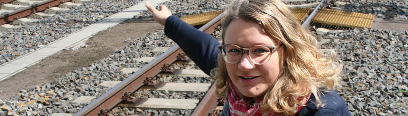 Gleis 2 im Bahnhof Dresden-Neustadt: Annegret Frenzel zeigt, wo die Kabelkanäle verlaufen. Eine Frau mit blonden Haaren und Brille hockt an einer Bahnschiene und zeigt auf etwas.