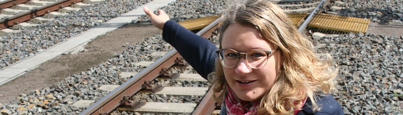 A TU Dresden graduate talks about her studies and career in the career choice magazine A woman with blond hair and glasses squats by a railway track and points at something.